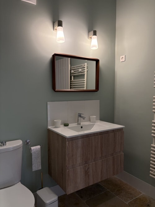 Vanité de salle de bain moderne avec tiroirs en bois, plan de travail blanc, armoire à pharmacie miroir et luminaires suspendus au Gîte