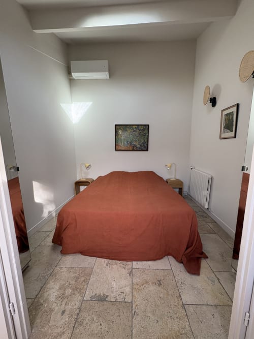 Chambre minimaliste au Gîte château de Pannis à Arles avec literie couleur rouille, carrelage et murs blancs ornés d'œuvres d'art.