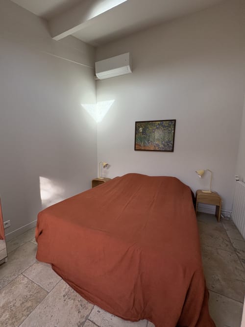 Chambre minimaliste au Gîte château de Pannis à Arles avec literie en terre cuite, tables de nuit en bois, décoration murale et climatisation