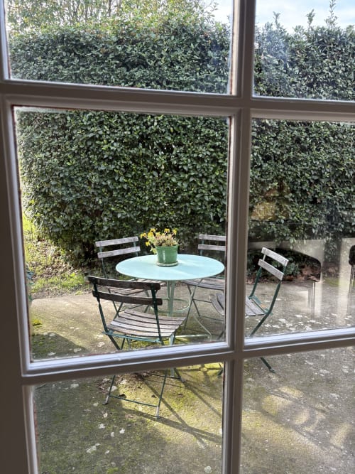 Vue par la fenêtre sur la terrasse du jardin avec table ronde et chaises au Gîte Château de Pannis, Arles