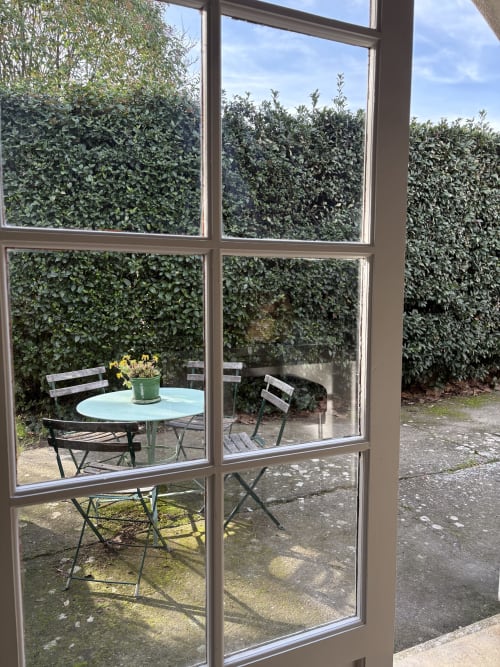 Vue sur le jardin à travers les portes vitrées du Gite Chateau de Pannis, Arles - terrasse extérieure avec table ronde et chaises