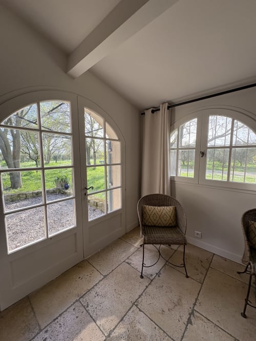 Solarium lumineux aux portes cintrées surplombant des jardins paysagers au Gite Château de Pannis, Arles, avec mobilier en rotin