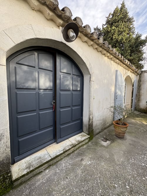 Portail voûté noir donnant accès au Gîte Château de Pannis à Arles, façade en pierre claire et toiture couverte de lierre