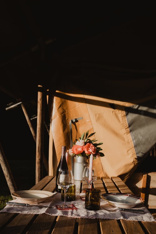 Installation dîner glamping aux gîtes de Cormenin : vin, fleurs et couverts sous tente toile