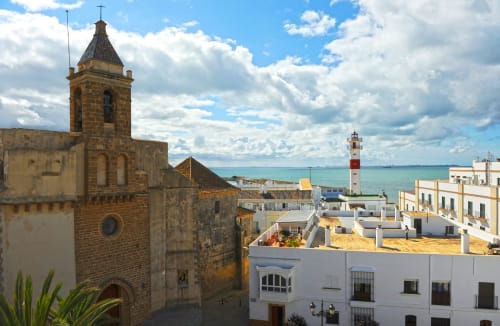 Torre de iglesia histórica con vistas a casas encaladas y el mar Mediterráneo en Rota, España, cerca del Hostal La Moyareja