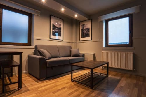 Modern lounge with gray sofa, wooden table, and framed photos at La Borda del Gato Rafa hotel in Vielha