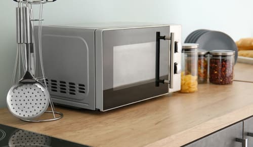 Microwave and kitchen utensils on wooden counter at La Borda del Gato Rafa hotel in Vielha, Spain