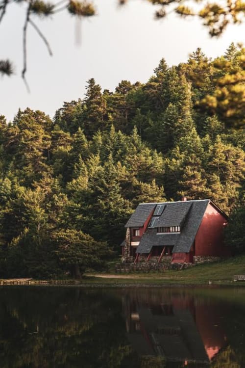 Red hotel building with dark roof nestled among evergreen trees beside a calm lake in Vielha, Spain