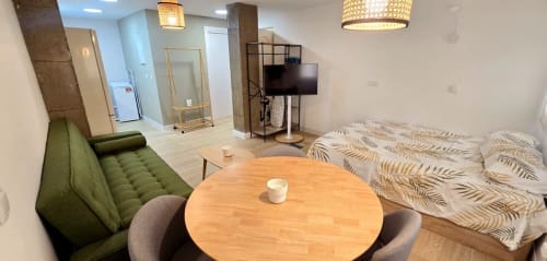 Moderno estudio en Murcia con mesa de comedor, sofá verde, cama con sábanas estampadas, TV y cocina americana