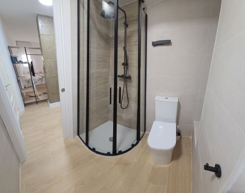 Baño moderno en apartamento del Hotel Numidas Open House Murcia con ducha amplia, inodoro blanco y piso con efecto madera