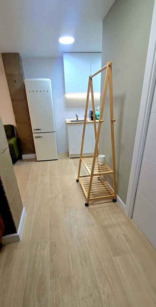 Pequeña cocina de estudio moderno con perchero de madera, refrigerador blanco y piso de madera clara en hotel de Murcia