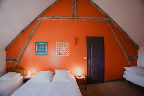 Chambre lumineuse aux tons d'orange vif aux Gîtes de Cormenin, avec literie blanche, poutres en bois et porte sombre