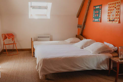 Chambre lumineuse à la villa Les gîtes de Cormenin avec literie blanche, mur d'accent orange, puits de lumière et vue sur le jardin