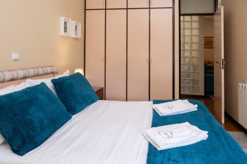 Quarto moderno no RH Charming Apartments em Braga com almofadas teal, lençol branco e móveis contemporâneos