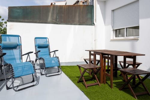 Pátio exterior do RH Charming Apartments em Braga com espreguiçadeiras azuis e mesa de piquenique em madeira sobre grama sintética