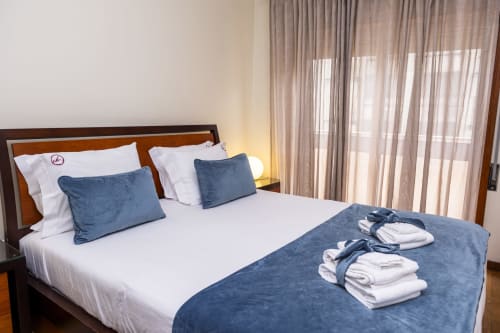 Quarto moderno de hotel nos RH Charming Apartments em Braga com almofadas azuis, roupa de cama branca e toalhas limpas