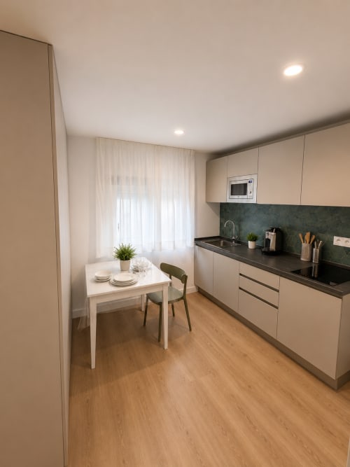 Moderne Studio-Küche und Essbereich im Fly High Morro Jable mit weißen Schränken, dunkler Arbeitsplatte, kleinem Tisch und Holz