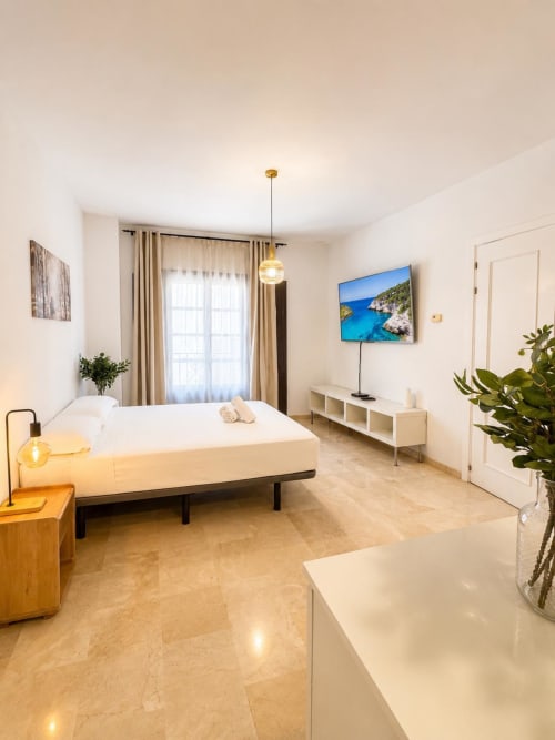 Moderno dormitorio en apartamento dúplex de Málaga con cama, televisor, escritorio de trabajo y plantas tropicales