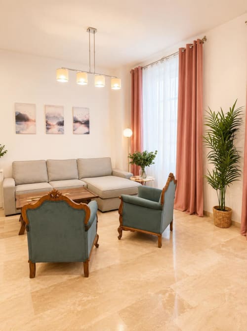 Moderno salón en apartamento de Málaga con sofá beige, butacas color turquesa, cortinas coral y planta decorativa