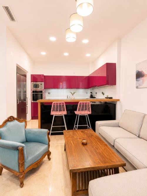 Moderno apartamento de planta abierta en Málaga con muebles de cocina rojo, mesa de comedor de madera, sillón azul y cómodo
