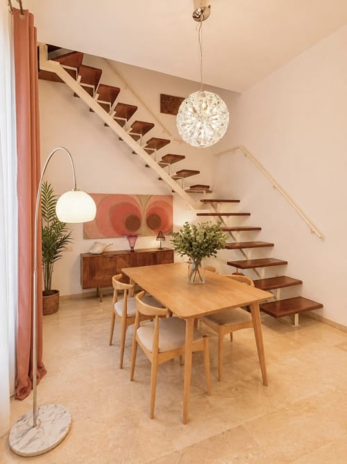 Comedor moderno en dúplex de Málaga con mesa de madera, sillas, escalera flotante e iluminación colgante