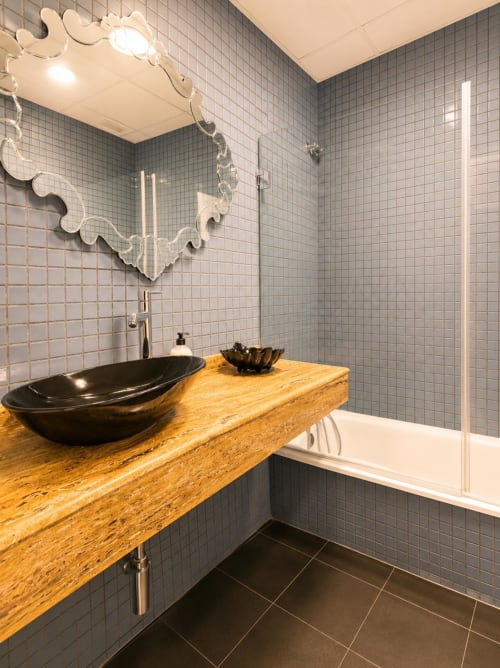 Baño moderno con azulejos grises, lavabo negro de cerámica sobre encimera de madera y cabina de ducha en Sinese Design Homes, Málaga