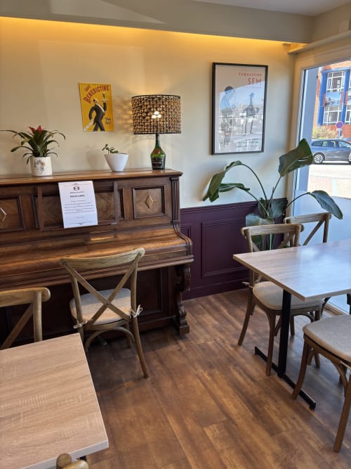 Salle de bistrot de l'Hôtel de la Poste à Saint-Valery-en-Caux avec tables en bois, piano et affiches vintage