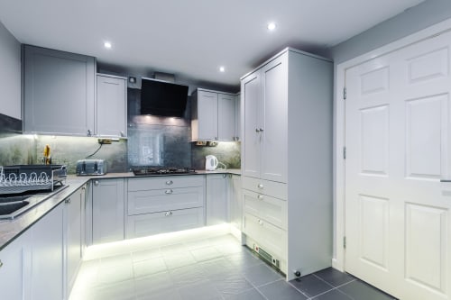 Modern fully equipped kitchen at Vidale Court villa in Manchester with white cabinetry, dark countertops, and integrated