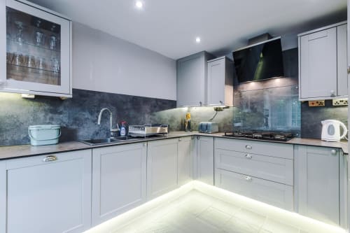 Modern kitchen in Vidale Court villa Manchester with white cabinets, dark tiled backsplash, stainless steel appliances and