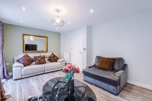 Modern living room at Vidale Court villa in Manchester with cream sofa, grey armchair, floral arrangement, and gold-framed