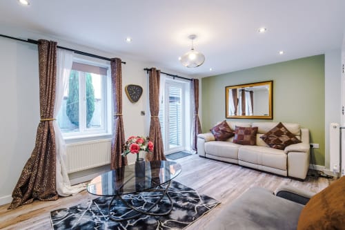 Bright modern living room at Vidale Court villa in Manchester with cream sofa, green walls, and floor-to-ceiling windows with