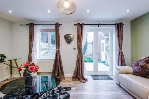 Modern living room at Vidale Court Manchester villa with brown curtains, cream sofa, glass table and garden views