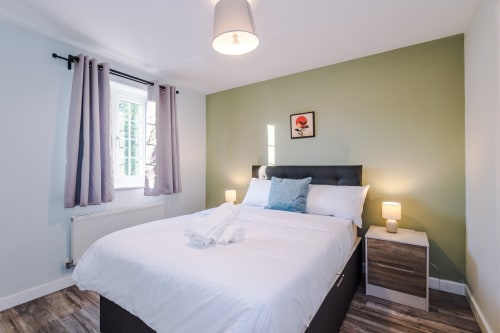 Bright bedroom at Vidale Court Manchester with green accent wall, black bed, purple curtains, bedside lamps, and wooden