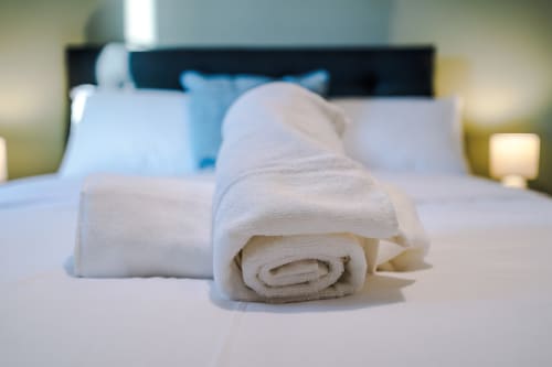 Rolled white towels on bed at Vidale Court villa in Manchester with pillows and headboard in background