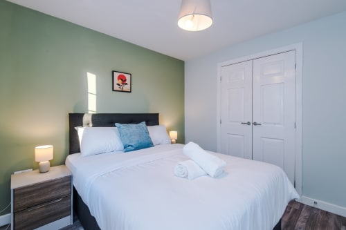 Modern bedroom at Vidale Court villa in Manchester with sage green walls, queen bed, blue pillows, and white closet doors