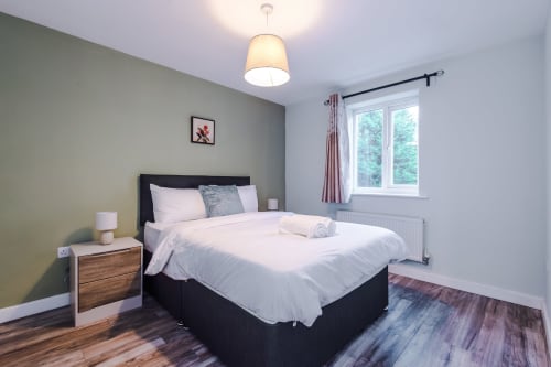 Modern bedroom at Vidale Court villa in Manchester with black bed, white bedding, wooden nightstand, pendant light, and large