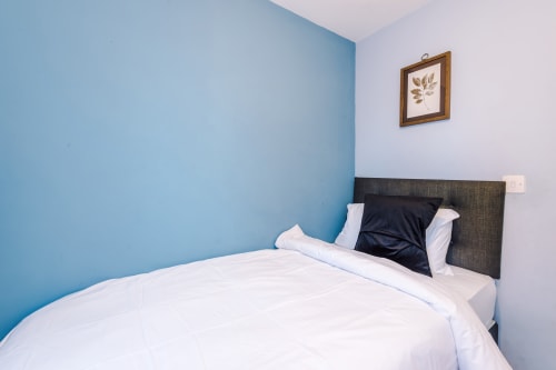 Modern bedroom at Vidale Court Manchester villa with blue accent wall, dark headboard, white bedding, and botanical wall art