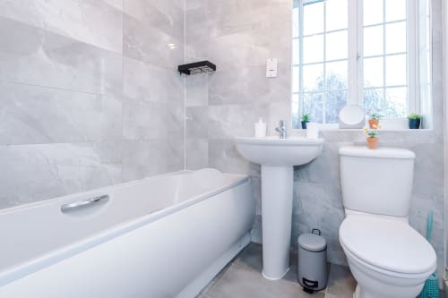 Modern bathroom at Vidale Court villa in Manchester with white suite, marble tiles, bathtub, pedestal sink, and toilet