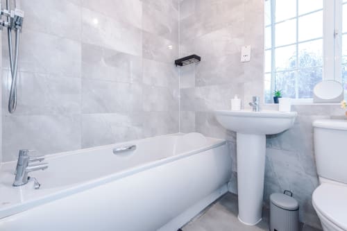 Modern bathroom at Vidale Court villa in Manchester with white bathtub, pedestal sink, toilet, and gray marble tiling