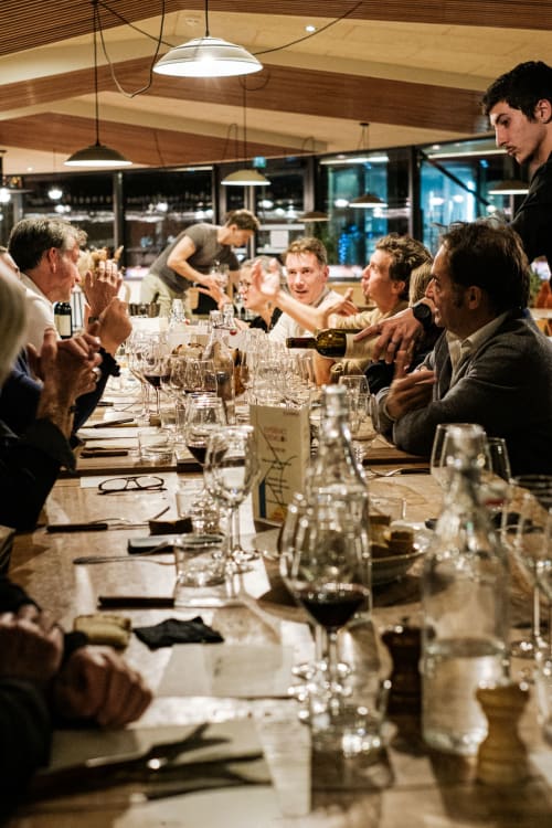 Huéspedes cenando juntos en el Hotel La Prison de Béziers, Francia, disfrutando de vino y conversación en un ambiente restaurante moderno.