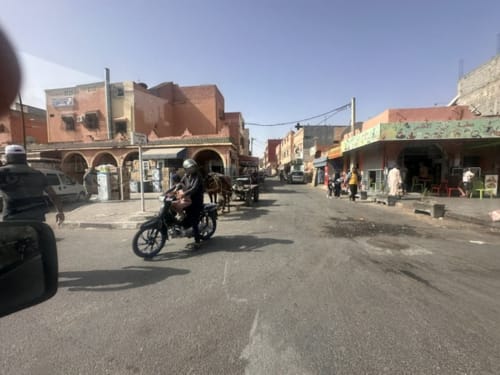 Rue marocaine animée à Essaouira avec motos, boutiques et bâtiments traditionnels en terre cuite