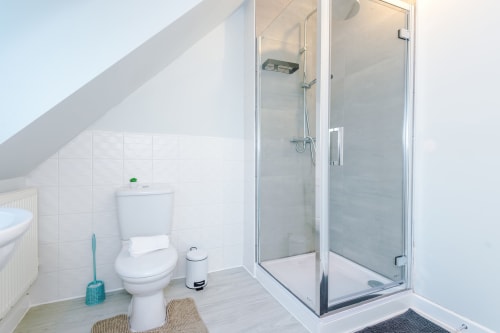 Modern bathroom in Vidale Court villa with toilet, shower enclosure, and white tile walls in Manchester