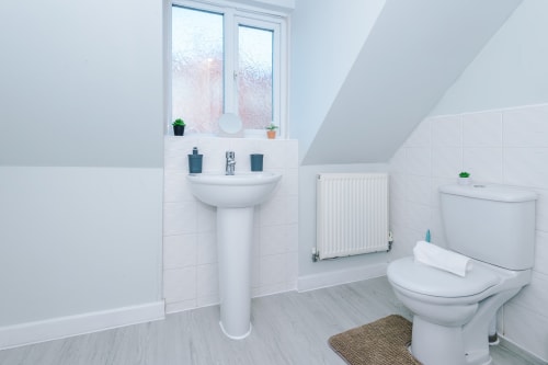 Modern bathroom at Vidale Court villa in Manchester with white pedestal sink, toilet, radiator, and tiled walls