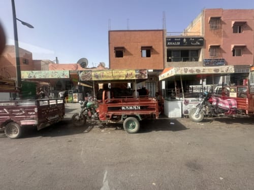 Scène de rue marocaine à El Ghazouane avec des camions de transport colorés et des bâtiments en briques traditionnels près d'Essaouira