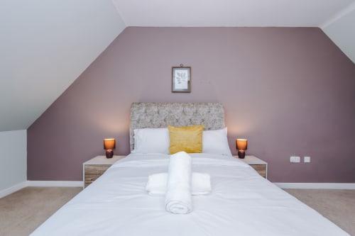 Modern bedroom at Vidale Court villa in Manchester with purple accent wall, neutral bedding, and yellow cushion