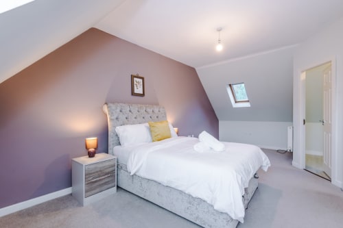 Modern attic bedroom at Vidale Court villa in Manchester with purple accent wall, queen bed, skylights, and ensuite door