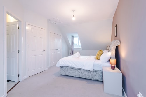 Bright modern bedroom at Vidale Court villa, Manchester with queen bed, white bedding, gold accent pillow, and white fitted