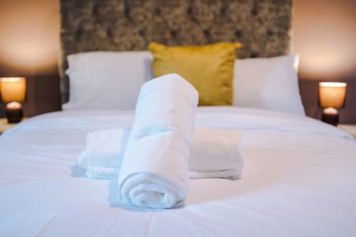 Rolled white towels on bed at Vidale Court villa in Manchester with pillows and yellow cushion