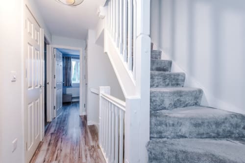 Bright hallway with staircase and gray carpet runner in a Manchester villa, white railings, wooden flooring