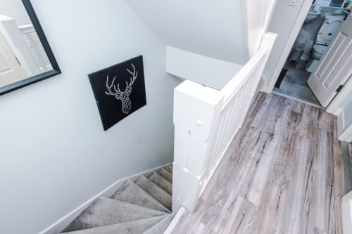 Modern staircase at Vidale Court villa in Manchester with gray carpet, white walls, wooden flooring, and black deer artwork